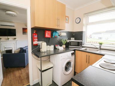 A kitchen with a washing machine microwave kettle and sink next to a window at Chalet 235 in Wilsthorpe near Bridlington