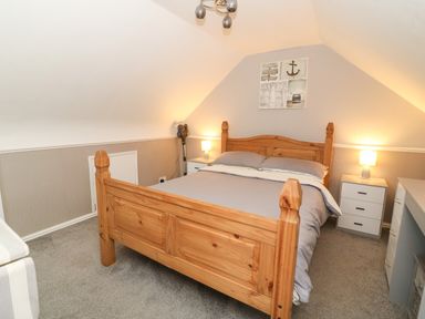 A bedroom with a wooden bed a grey bedspread two bedside tables with lamps and a wall painting at Chalet 235 Wilsthorpe near Bridlington