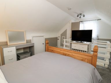 A bedroom with a wooden bed, a desk with a mirror, a television on a cabinet, and a window with curtains at Chalet 235 Wilsthorpe near Bridlington