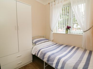 A small bedroom with a single bed with striped bedding a white wardrobe and a window with white curtains and flowers on the sill at Chalet 235 Wilsthorpe near Bridlington