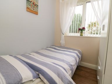 A small bedroom with a bed striped bedding and a window with curtains and flowers on the sill at Chalet 235 Wilsthorpe near Bridlington