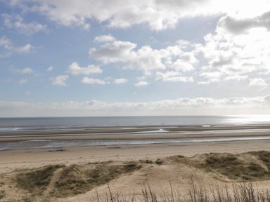 A sandy beach with grassy dunes and water channels under a cloudy sky at Chalet 235 Wilsthorpe near Bridlington