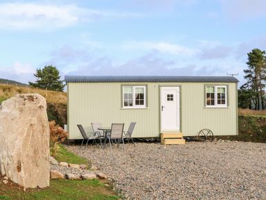 A small light green cabin with two windows and a white door with steps outside and a glass table with four chairs on a gravel area at Shepherds Retreat Glenlark Gortin near Greencastle