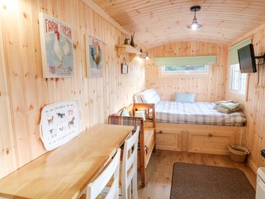 A small wooden room with a bed a table two chairs wall art and a mounted television at Shepherds Retreat Glenlark in Gortin near Greencastle