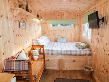 A small wooden room with a bed that has plaid bedding and folded towels a wooden bench with a lamp and pillow a wall-mounted tv and small windows at Shepherds Retreat Glenlark Gortin near Greencastle