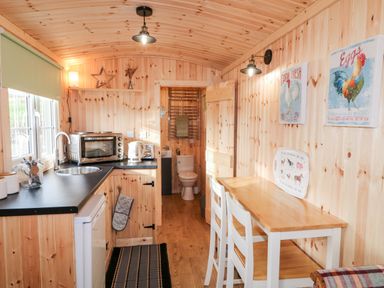 A small kitchen and dining area with wooden walls and ceiling a sink microwave kettle toaster small dining table with two chairs at Shepherds Retreat Glenlark Gortin near Greencastle