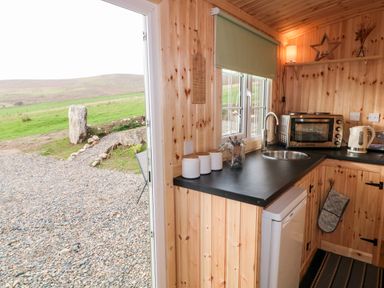 A small wooden kitchen with a window a countertop with jars a toaster oven and kettle at Shepherds Retreat Glenlark in Gortin near Greencastle