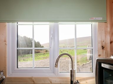 A kitchen window with a faucet and part of a microwave showing a rural landscape at Shepherds Retreat Glenlark Gortin near Greencastle