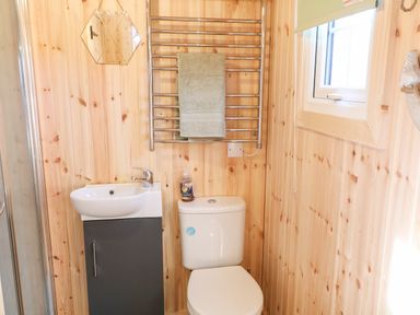 A bathroom with a toilet, small sink with cabinet, towel rack with towel, and window at Shepherds Retreat Glenlark Gortin near Greencastle