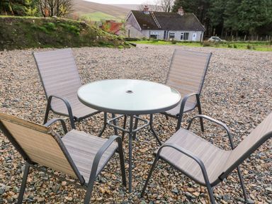 An outdoor seating area with four chairs and a round glass table on a gravel surface at Shepherds Retreat Glenlark in Gortin near Greencastle