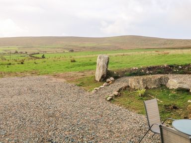 A gravel area with a glass table and two chairs near a grassy field with large rocks at Shepherds Retreat Glenlark in Gortin near Greencastle