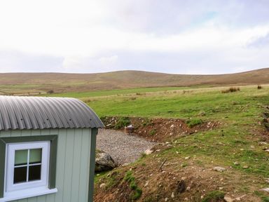A small green structure with a window near a gravel area and open grassy hills at Shepherds Retreat Glenlark in Gortin near Greencastle