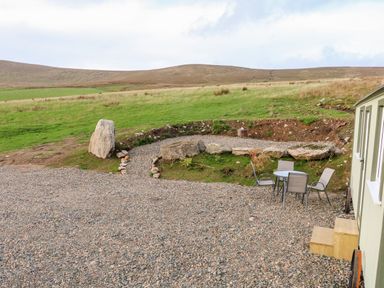 An outdoor area with gravel ground table and chairs a green hill in the background at Shepherds Retreat Glenlark Gortin near Greencastle