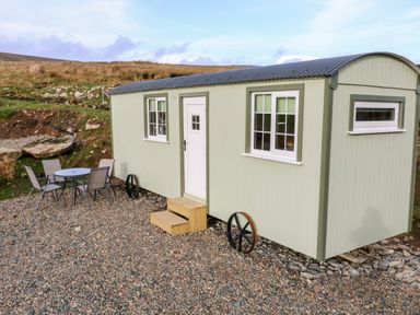 A small light green cabin with white windows and a door on a gravel area with a round table and four chairs outside at Shepherds Retreat Glenlark in Gortin near Greencastle
