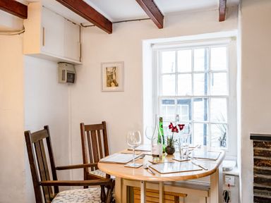 A dining area with a wooden table set for four near a window at Honey Cottage in Port Isaac
