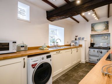A kitchen with white cabinets wooden countertops washing machine microwave and a stove at Honey Cottage in Port Isaac