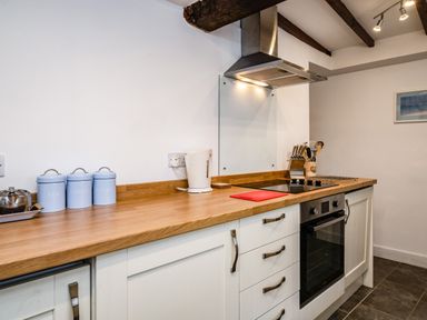 A kitchen with wooden countertop white cabinets electric stove kettle and canisters at Honey Cottage in Port Isaac