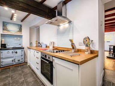 A kitchen with a wooden countertop white cabinets an electric stove oven and vintage blue cooker at Honey Cottage in Port Isaac