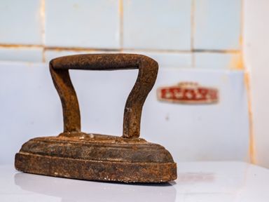 A rusty old flat iron placed on a white surface with tiled walls in the background at Honey Cottage in Port Isaac