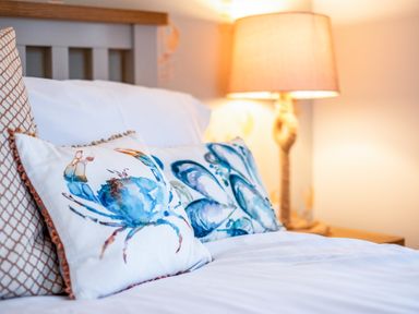 A bed with white pillows featuring blue crab and shell designs and a lamp in the background at Honey Cottage in Port Isaac