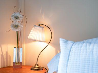 A bedside table with a lamp and a vase with flowers next to a bed at Honey Cottage in Port Isaac