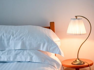 A bed with white pillows and sheets next to a wooden side table with a lamp at Honey Cottage in Port Isaac