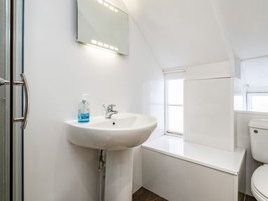 A bathroom with a sink soap dispenser mirror toilet and window at Honey Cottage in Port Isaac