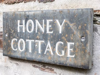A metal sign with the words Honey Cottage mounted on a stone wall at Honey Cottage in Port Isaac
