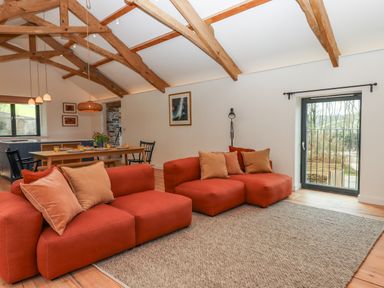 A living room and dining area with two orange sofas a wooden dining table under exposed wooden beams at 3 Caddaford Barns in Buckfastleigh
