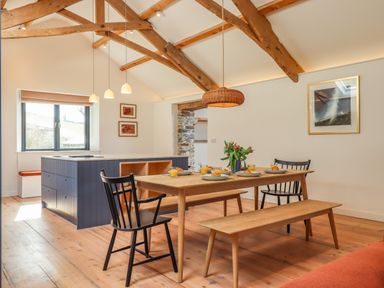 A dining area with wooden table chairs and bench under exposed wooden ceiling beams at 3 Caddaford Barns in Buckfastleigh