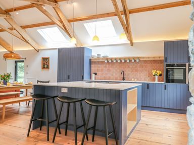 A kitchen with blue cabinets a kitchen island with black stools wooden beams on the ceiling and skylights at 3 Caddaford Barns in Buckfastleigh