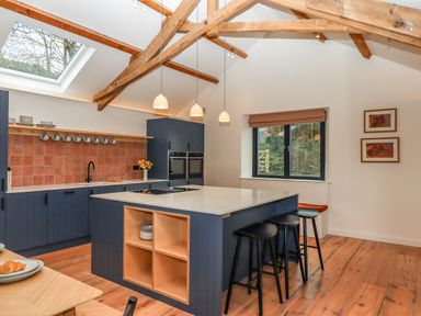A kitchen with a large island and bar stools under wooden beams at 3 Caddaford Barns in Buckfastleigh