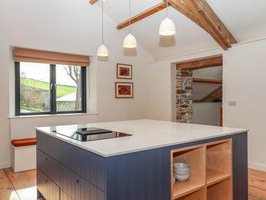 A kitchen with a central island, pendant lights, window with blind, and exposed wooden beams at 3 Caddaford Barns in Buckfastleigh