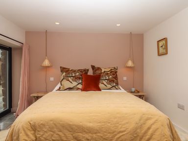 A bedroom with a bed featuring patterned pillows and a yellow bedspread at 3 Caddaford Barns in Buckfastleigh