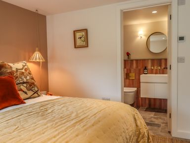 A bedroom with a bed and bedside lamp next to a bathroom entrance at 3 Caddaford Barns in Buckfastleigh