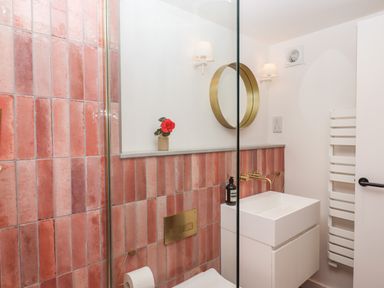 A bathroom with pink tiles a white sink a round mirror and a toilet at 3 Caddaford Barns in Buckfastleigh