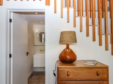 A hallway with a wooden chest of drawers and a lamp next to a door leading to a bathroom at 3 Caddaford Barns in Buckfastleigh