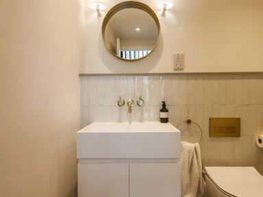 A bathroom sink with a round mirror above and a toilet with a towel ring at 3 Caddaford Barns in Buckfastleigh