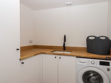 A utility room with a washing machine a sink with a black faucet wooden countertops and white cabinets at 3 Caddaford Barns in Buckfastleigh