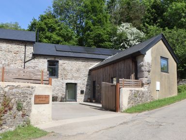 A stone building with solar panels on the roof and a wooden gate at 3 Caddaford Barns in Buckfastleigh