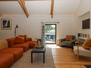 A living room with orange and gray seating wooden beams and a black coffee table at 3 Caddaford Barns in Buckfastleigh