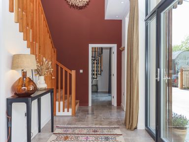 An entrance hallway with wooden staircase a console table with a lamp and vase a patterned rug and glass doors at 3 Caddaford Barns in Buckfastleigh