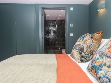 A bedroom with patterned pillows and an orange throw facing a door to a bathroom with dark tiles at 3 Caddaford Barns in Buckfastleigh