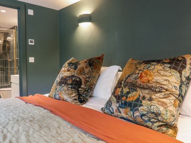 A bedroom with a bed with decorative pillows orange bed runner and a bathroom visible through a doorway at 3 Caddaford Barns in Buckfastleigh