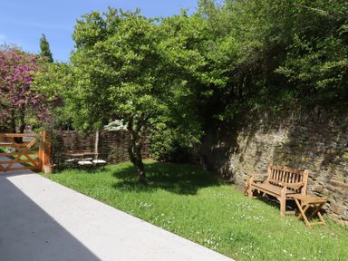A garden with a wooden bench and table set near a stone wall and a tree at 3 Caddaford Barns in Buckfastleigh