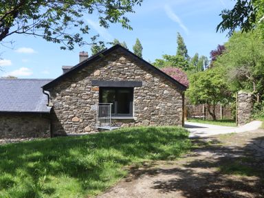 A stone house with a slate roof surrounded by trees and grass at 3 Caddaford Barns in Buckfastleigh