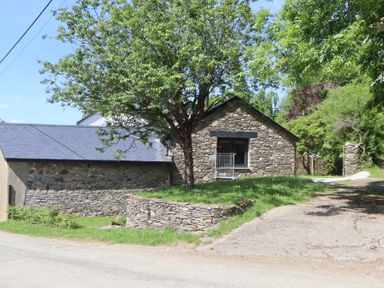 A stone building with a slate roof next to a tree and a small grassy area at 3 Caddaford Barns in Buckfastleigh