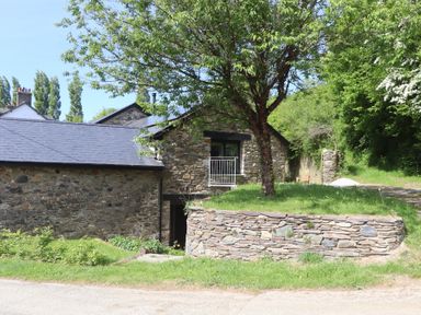 A stone building with a slate roof and a tree on a raised stone planter at 3 Caddaford Barns in Buckfastleigh
