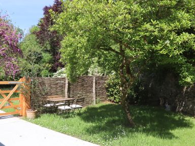 A garden with a tree a wooden gate a wicker fence a table and chairs with cushions at 3 Caddaford Barns Buckfastleigh
