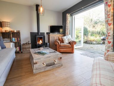 A living room with a wood stove a leather armchair a wooden coffee table and an open door to a garden at The Croft in Newport Pembrokeshire